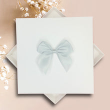 Load image into Gallery viewer, A white square box with a light blue bow on top, placed on a pink background.