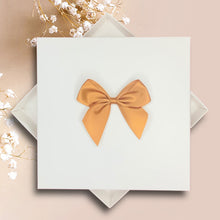 Load image into Gallery viewer, A white square box with a gold bow on top, placed on a pink background.
