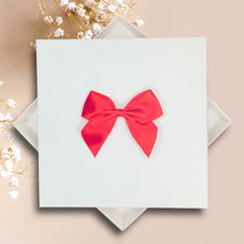 Load image into Gallery viewer, A white square box with a red satin bow on top, placed on a beige background.