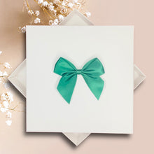 Load image into Gallery viewer, A white square card with a green bow on it, placed on a pink background.