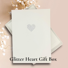 Load image into Gallery viewer, A white card with a heart-shaped glitter design on it, placed on a pink background.