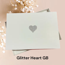 Load image into Gallery viewer, A white box with a silver glitter heart symbol on it, placed on a pink background.