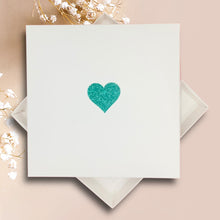 Load image into Gallery viewer, A white square card with a green glitter heart symbol in the center, placed on a pink background.
