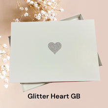 Load image into Gallery viewer, A white box with a silver glitter heart symbol on it, placed on a pink background.
