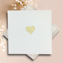 Load image into Gallery viewer, A white square card with a gold glitter heart design is placed on a pink background.
